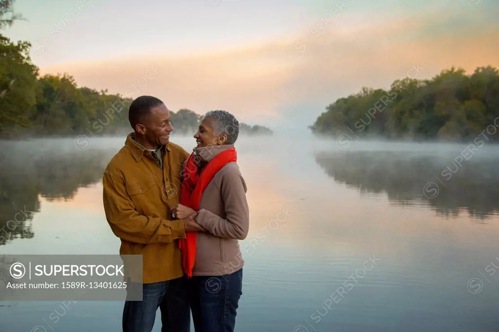 Older couple hugging at foggy river at sunrise