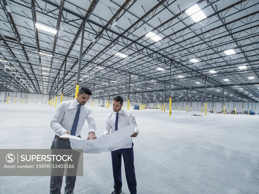 Architects examining blueprint in empty warehouse