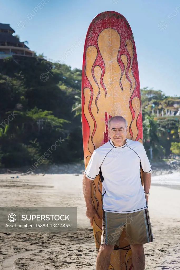 Older Hispanic man with surfboard on beach