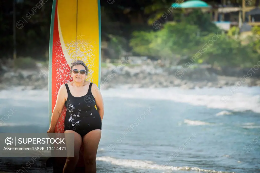 Older Hispanic woman with surfboard on beach