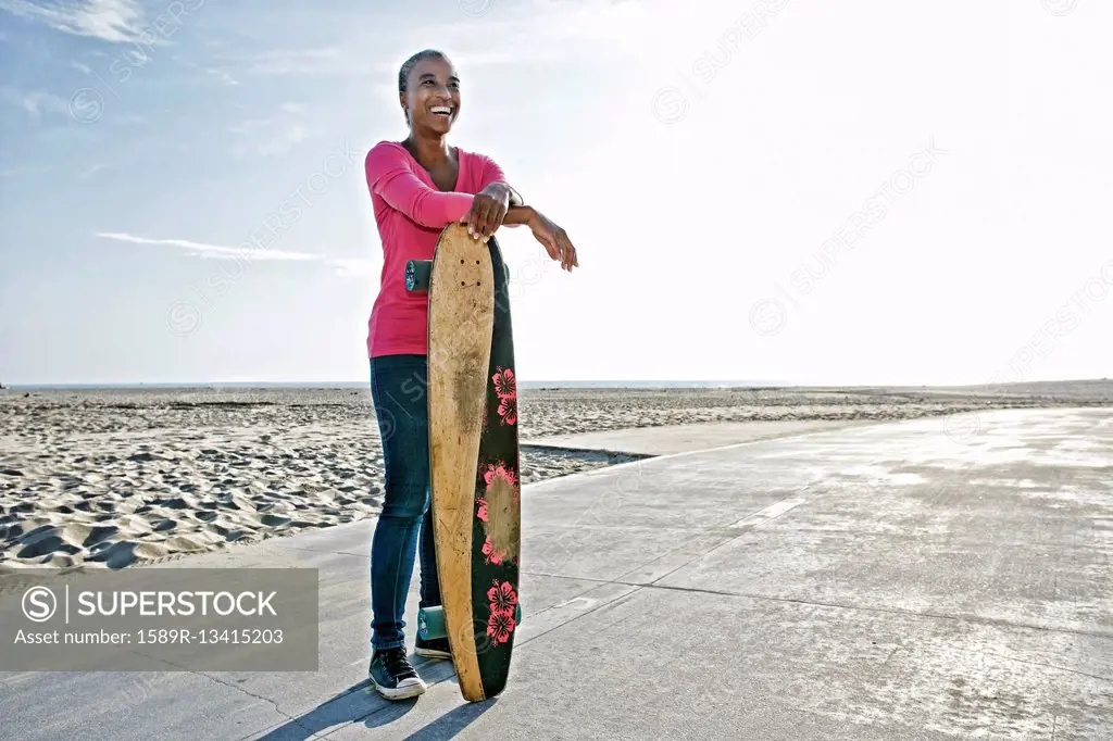 Older Black woman holding skateboard on beach