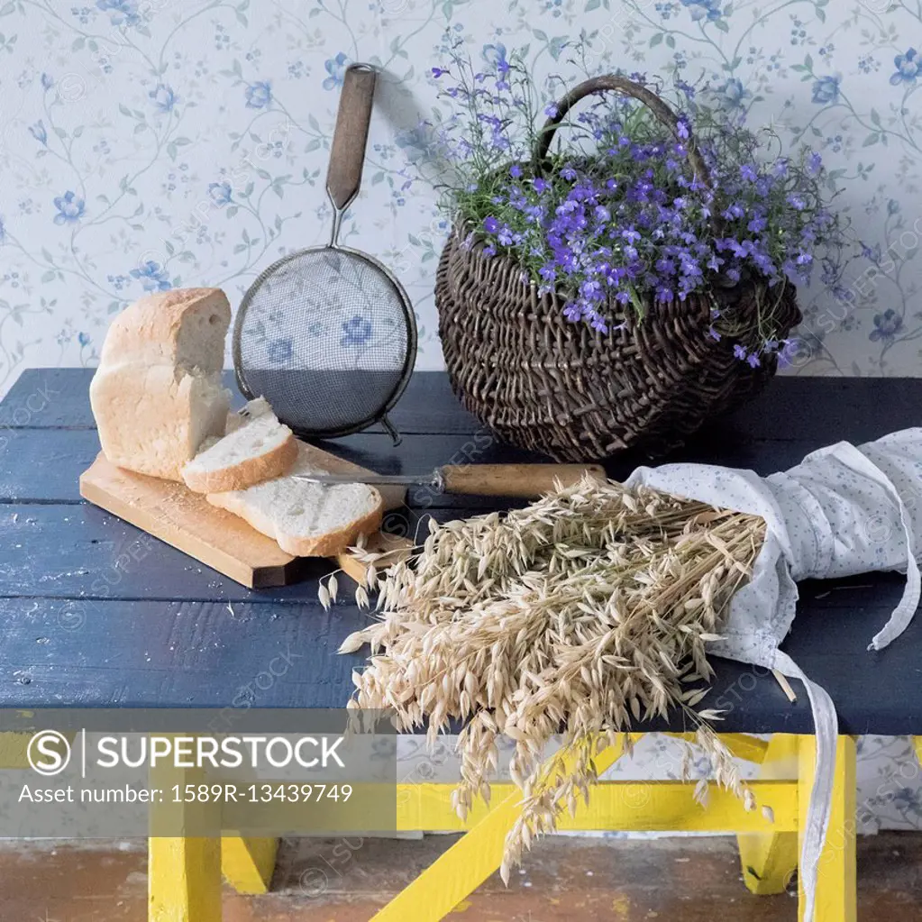 Wheat, sliced bread, sieve and flowers on bench