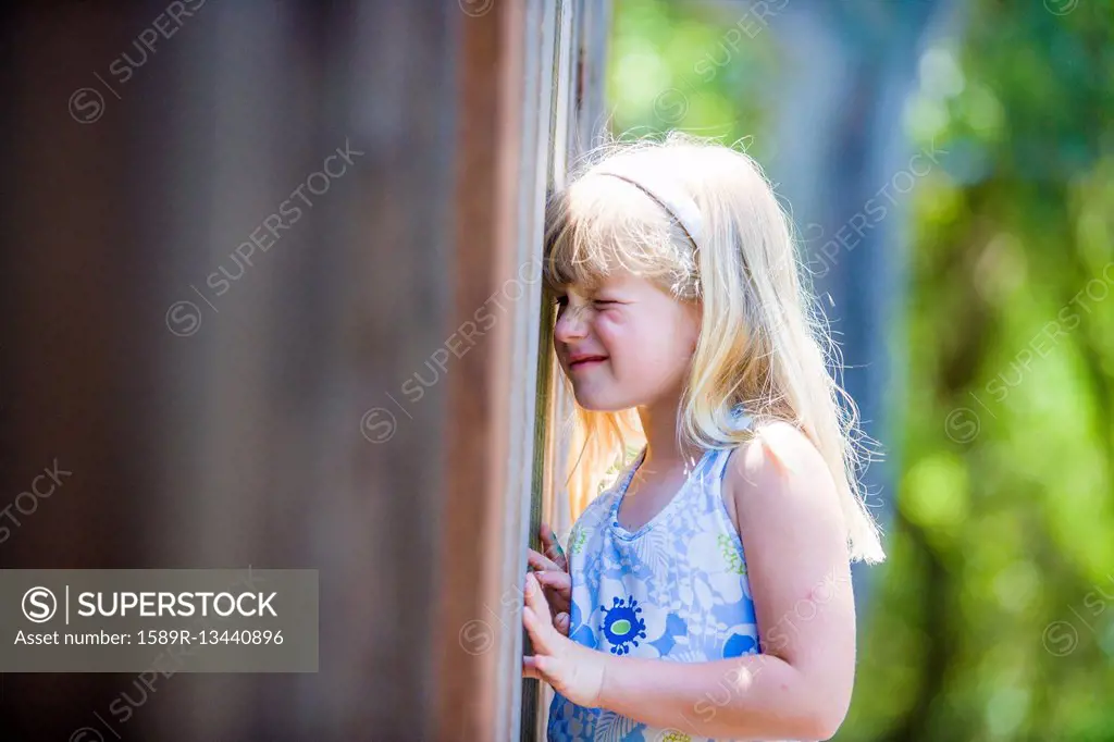 Curious Caucasian girl peeking through wooden fence