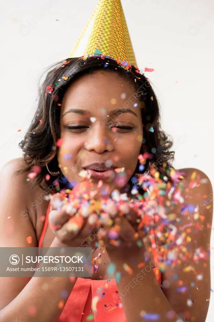 Mixed Race woman wearing party hat blowing confetti