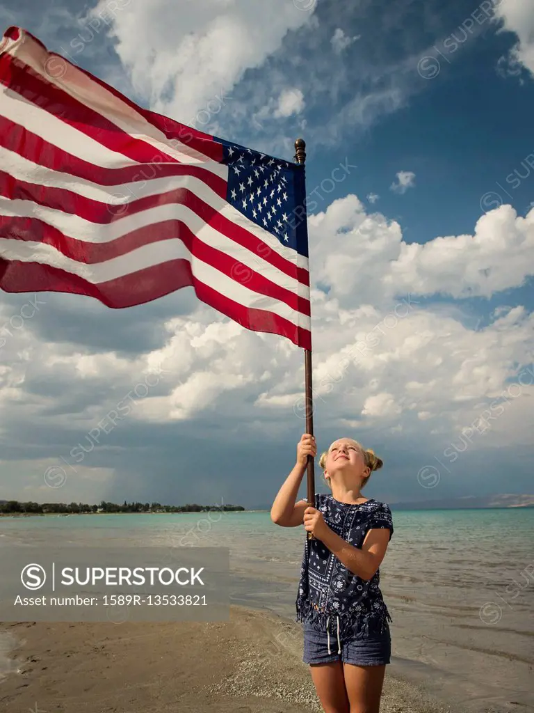 Caucasian girl holding American flag at beach