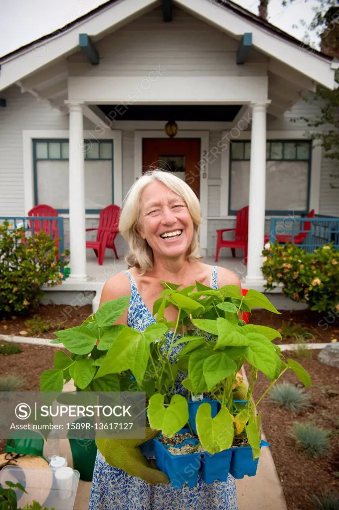 Portrait of smiling Caucasian woman holding tray of plants near house