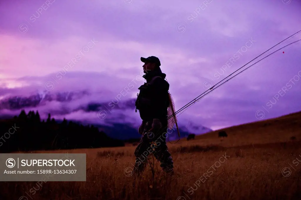 Caucasian man walking and carrying fishing rods