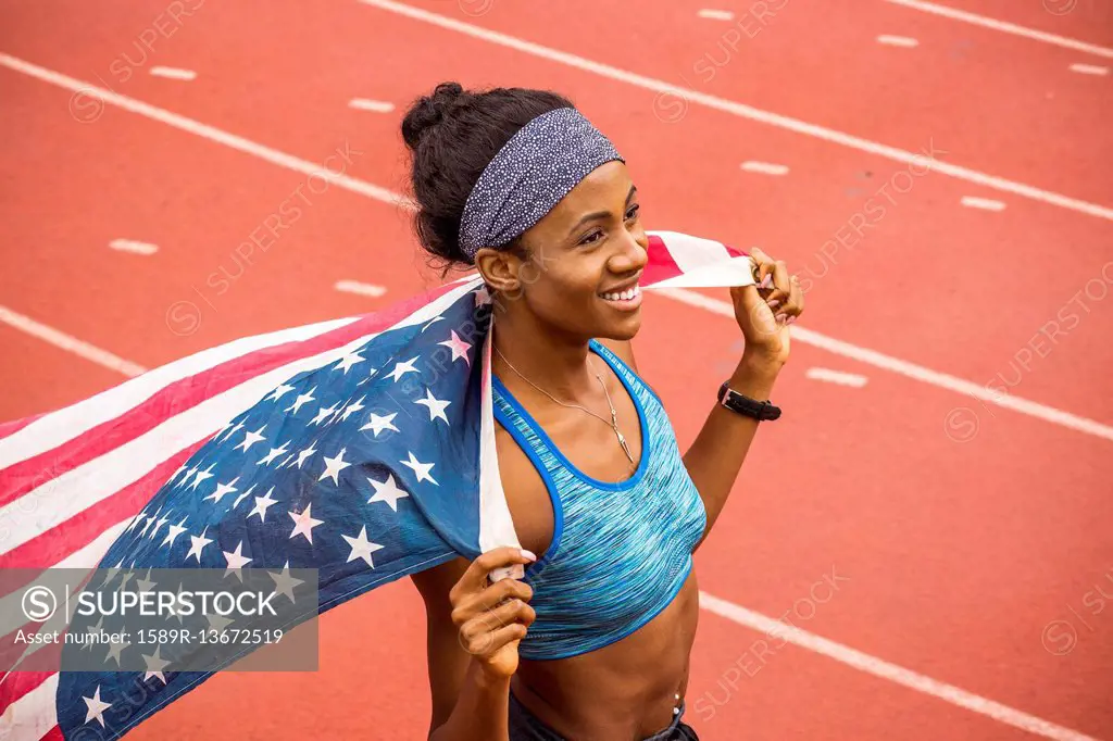 Smiling Black athlete holding American flag on track