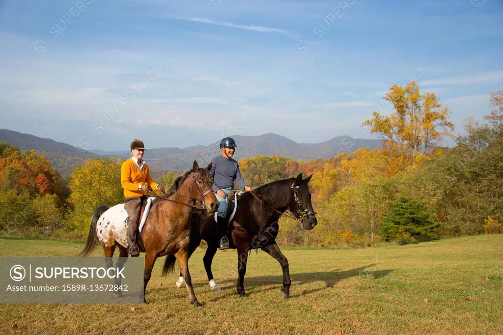 Older Caucasian couple horseback riding in field