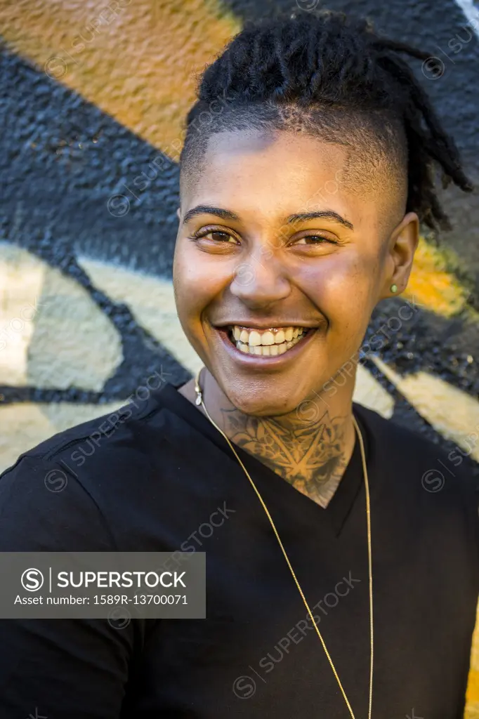 Portrait of androgynous Mixed Race woman smiling near graffiti wall