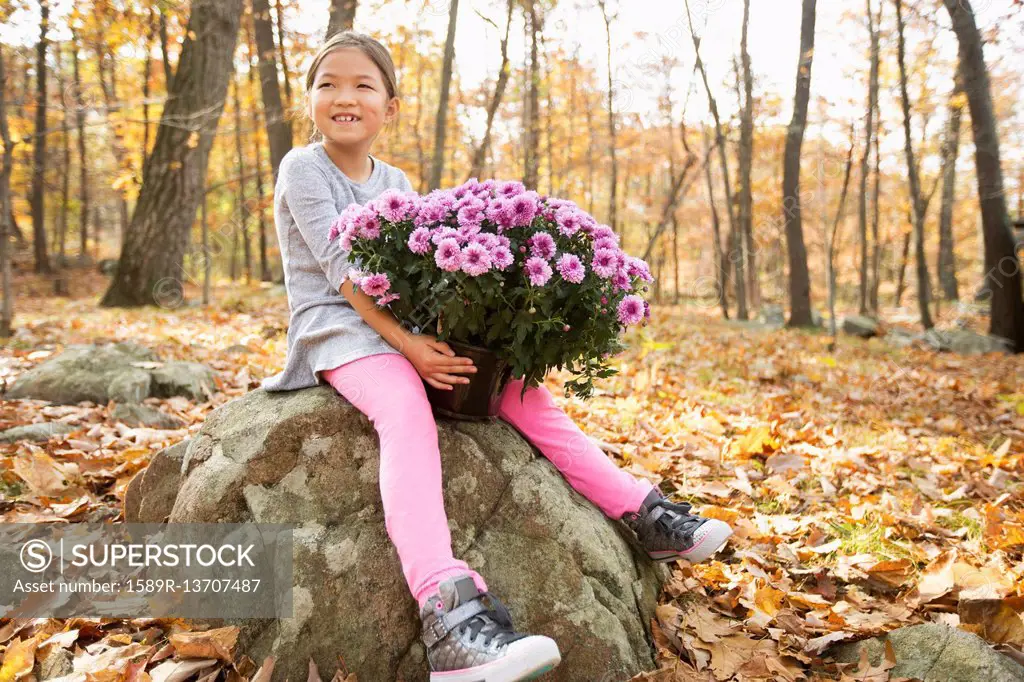 Smiling Mixed Race girls sitting on rock in autumn holding flowers
