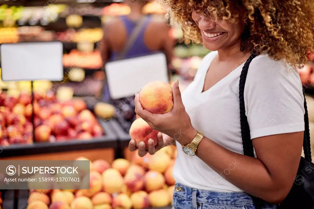 Black woman examining peaches in grocery store