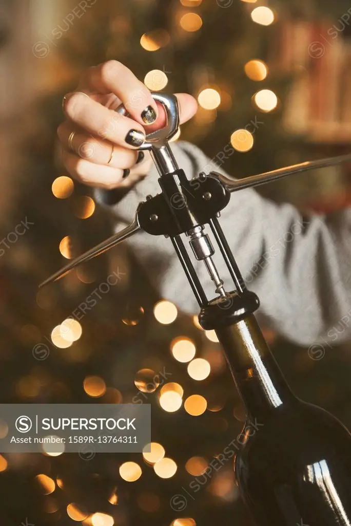 Hand of Caucasian woman opening wine bottle with corkscrew