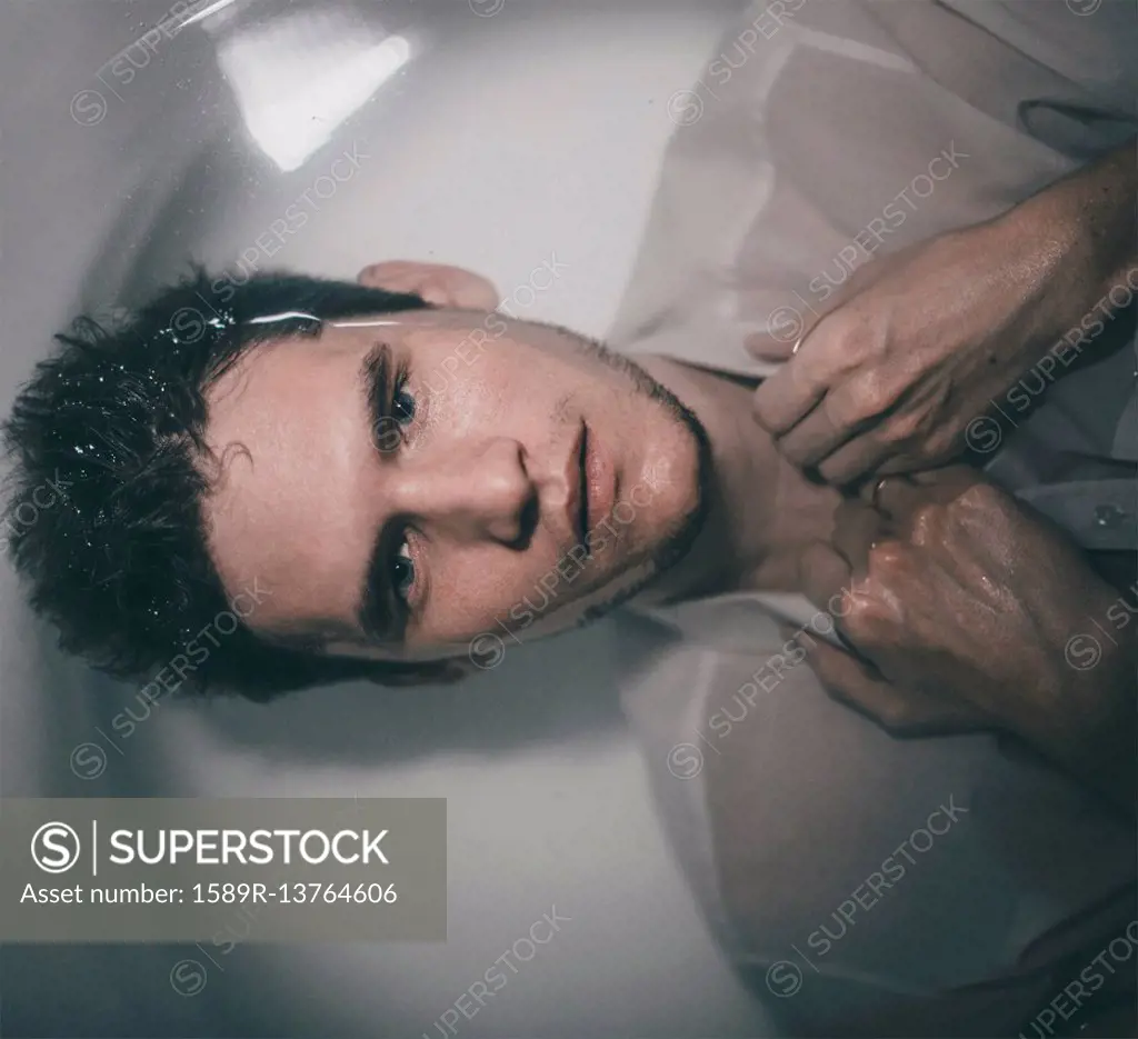 Caucasian man wearing shirt laying underwater in bathtub