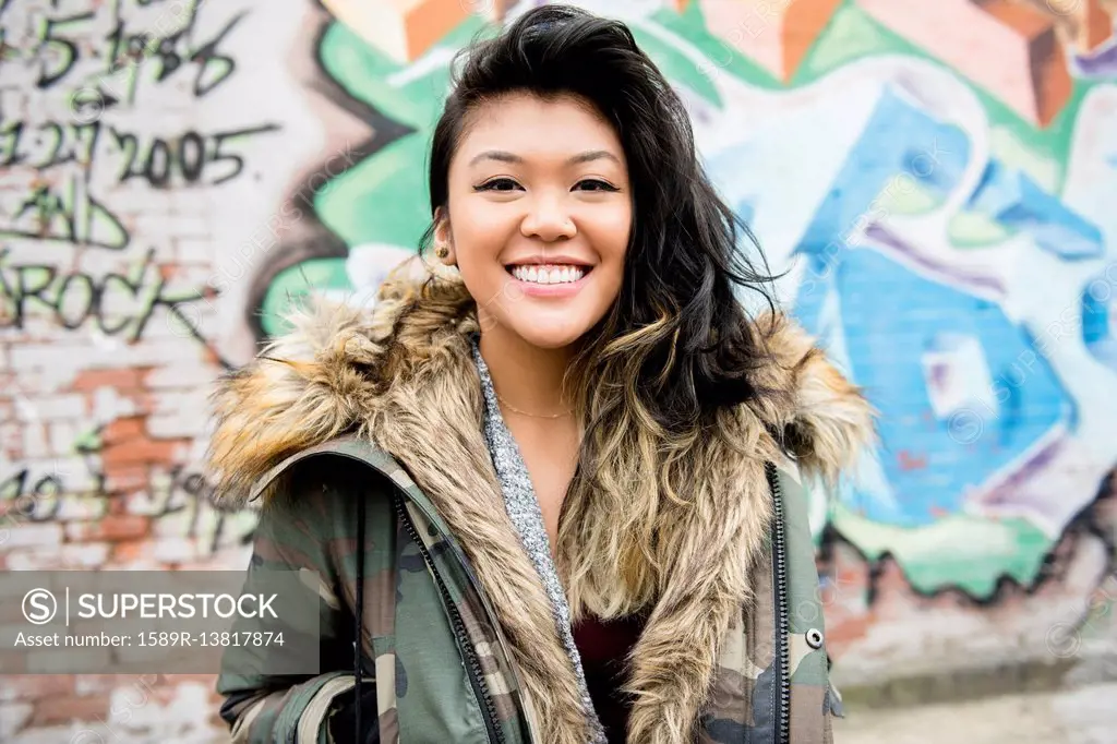 Portrait of smiling Mixed Race woman standing near graffiti