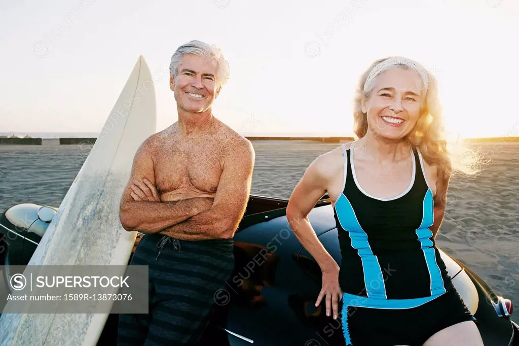 Older Caucasian couple leaning on convertible car with surfboards