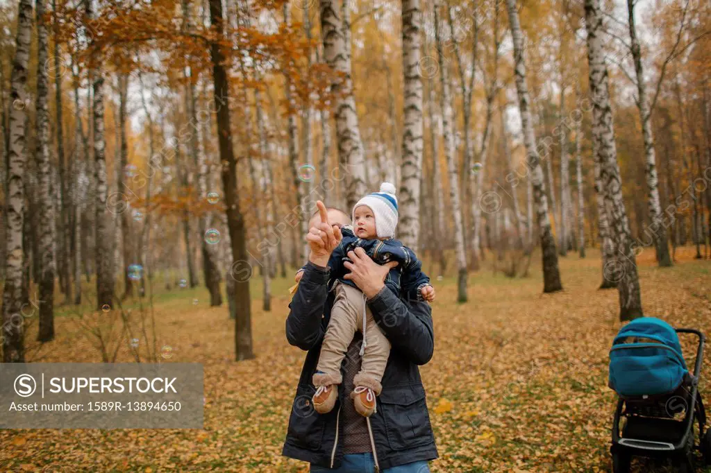 Middle Eastern father holding baby son and pointing in autumn