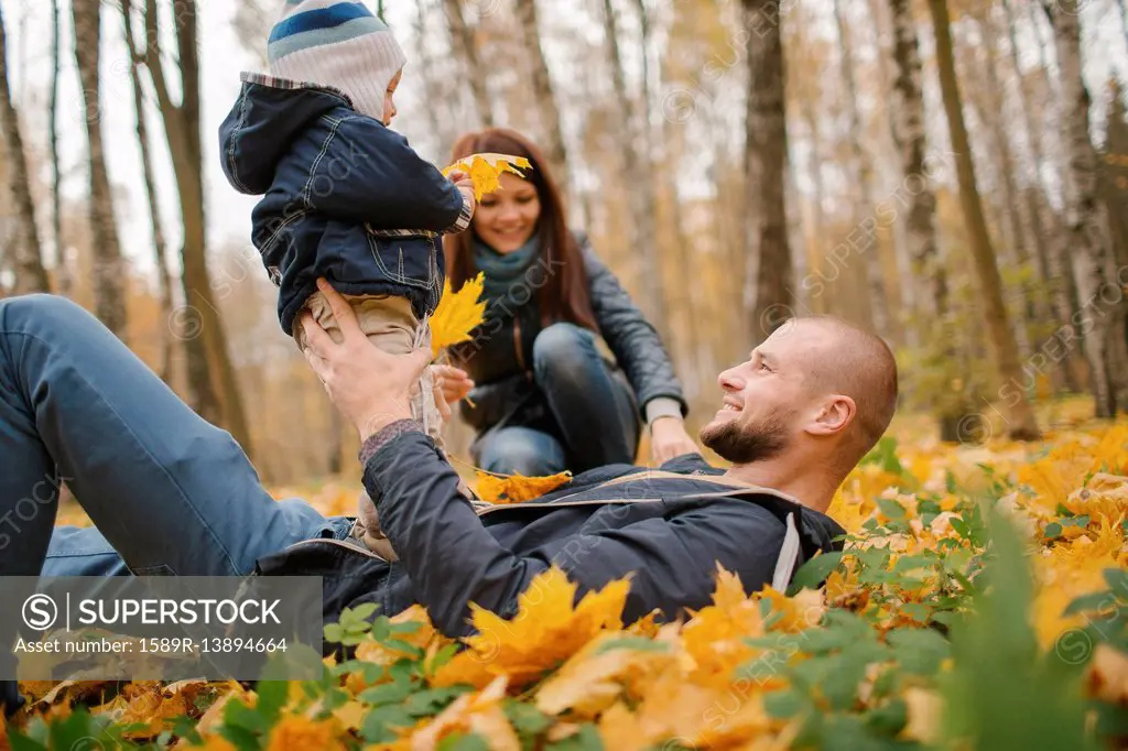 Middle Eastern father laying in autumn leaves holding baby son