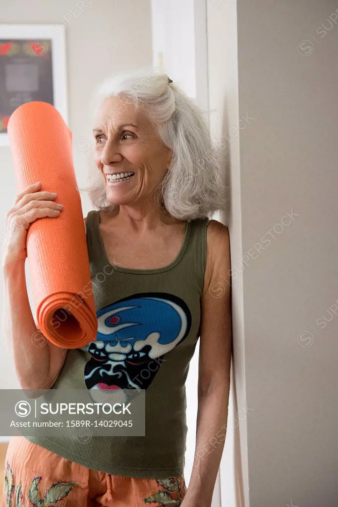 Older woman leaning on wall holding exercise mat