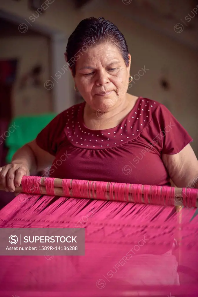 Hispanic woman weaving fabric on loom