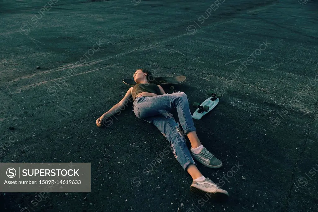 Caucasian teenage girl laying on pavement with head on skateboard