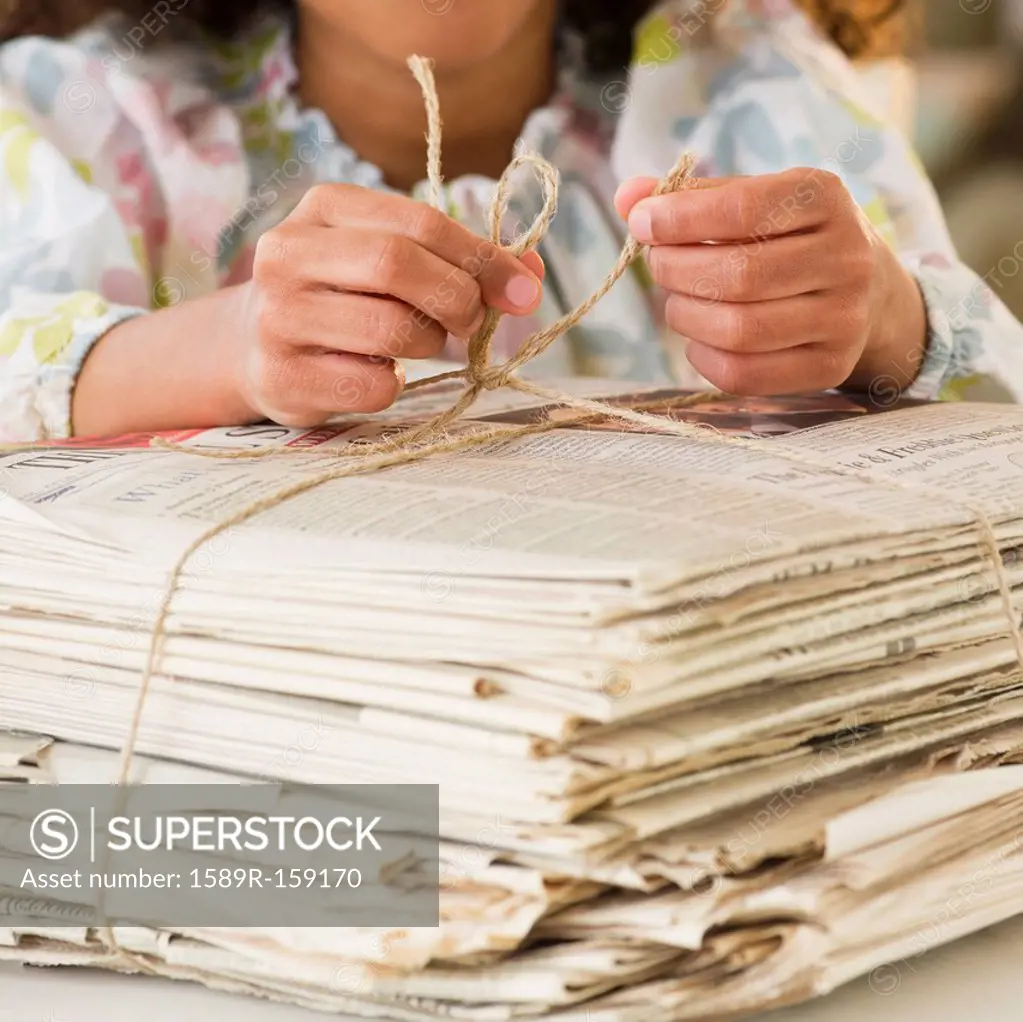 Mixed race girl tying bundle of newspapers