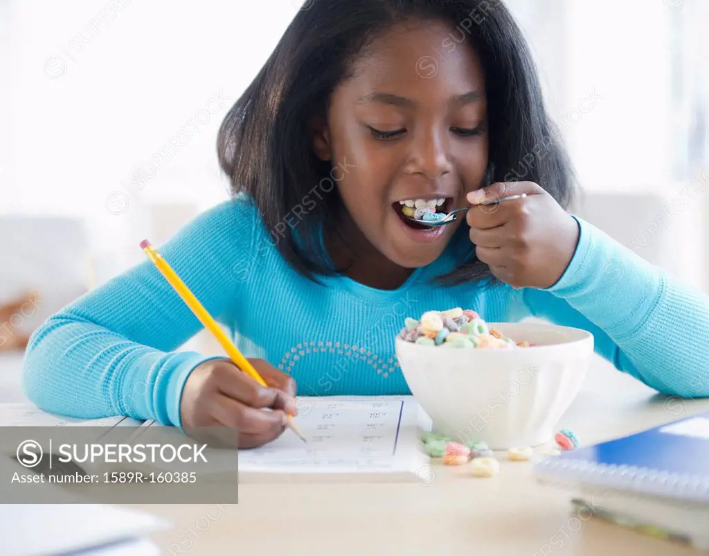 Black girl eating cereal and writing in workbook