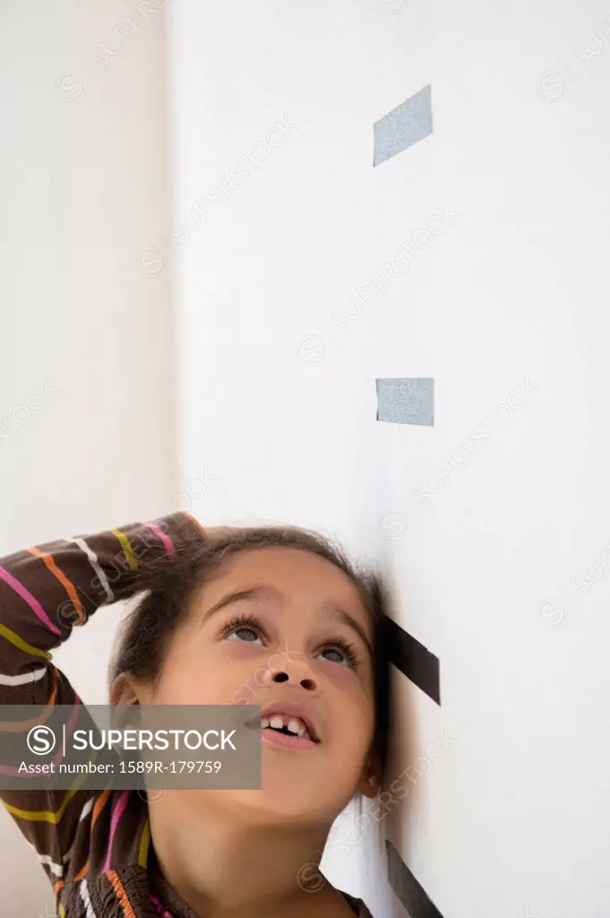 Hispanic girl measuring her height on wall