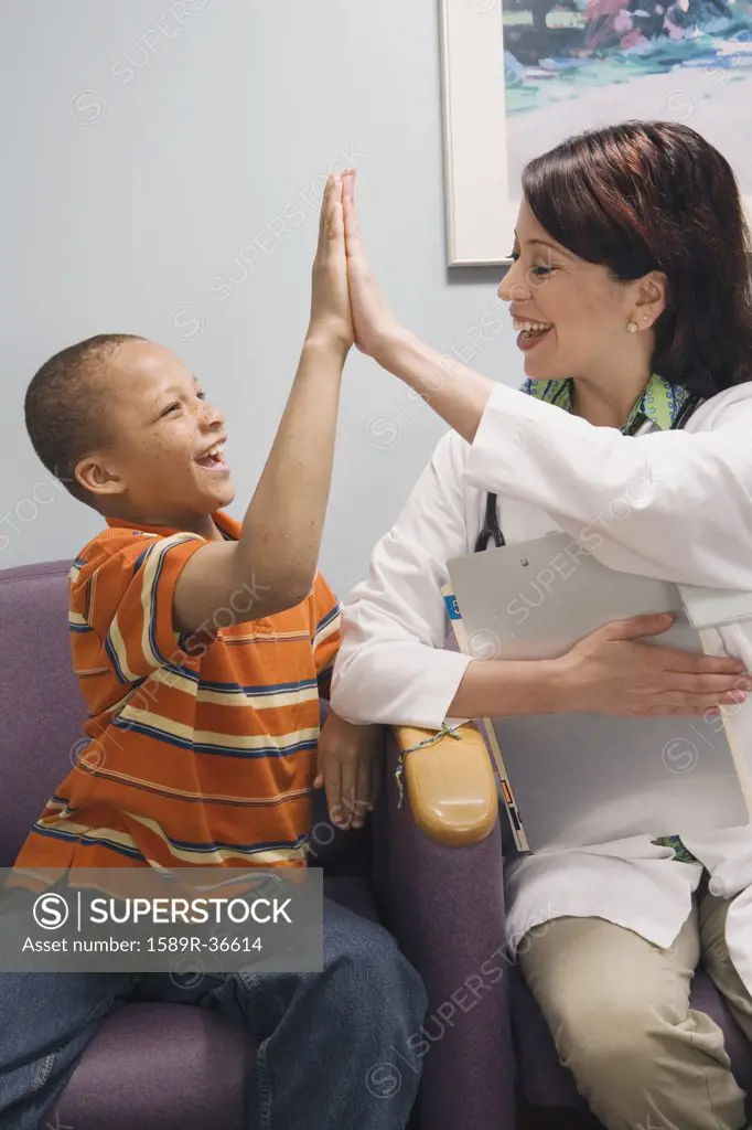 African boy and Hispanic female doctor high-fiving in waiting room