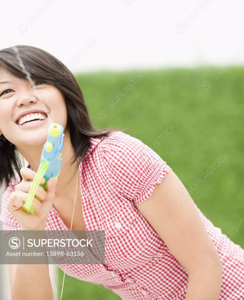 Asian woman squirting toy water gun - SuperStock