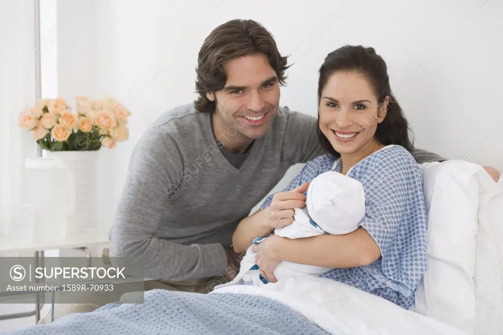 Hispanic couple holding newborn baby in hospital bed