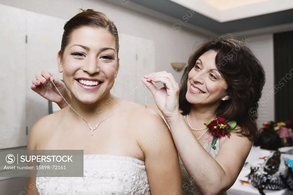 Bride's mother putting necklace on daughter