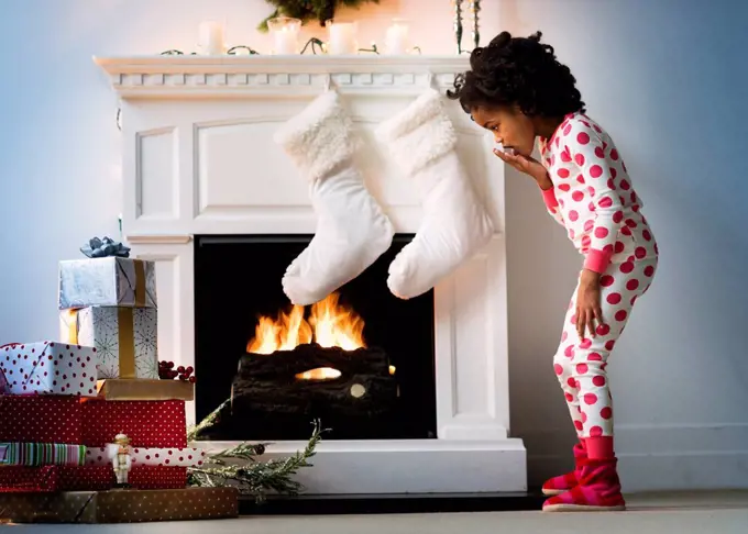 Surprised Black girl in pajamas looking down at Christmas gifts