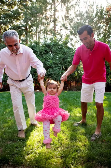 Father and grandfather helping daughter walk in backyard