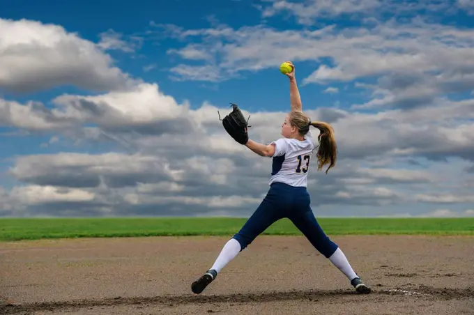 Caucasian softball player pitching ball in field