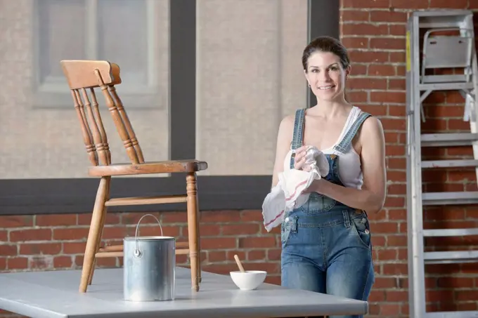 Mixed race woman painting chair in loft