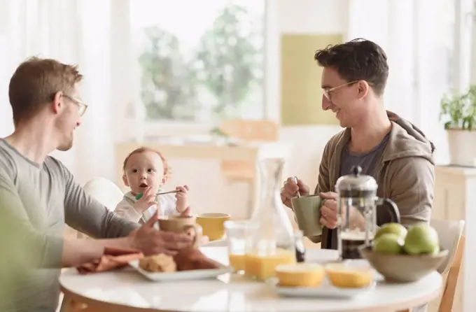 Caucasian gay fathers and baby eating breakfast