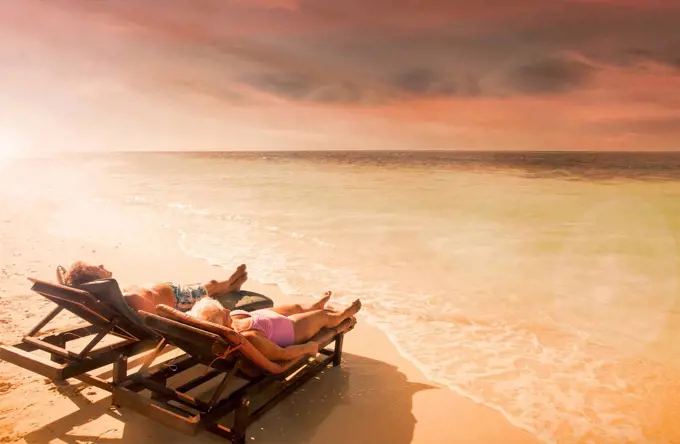 Older Caucasian couple relaxing on beach at sunset