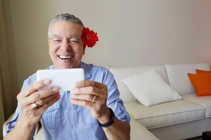 Older Black man taking selfie with flower behind his ear