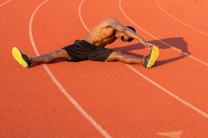 Black athlete stretching on track in sports field