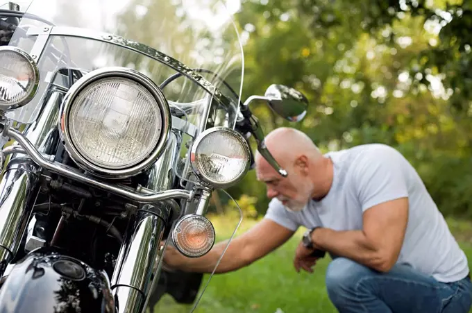 Older man repairing motorcycle in park