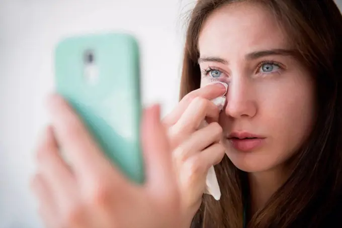 Native American woman with cell phone wiping away tears