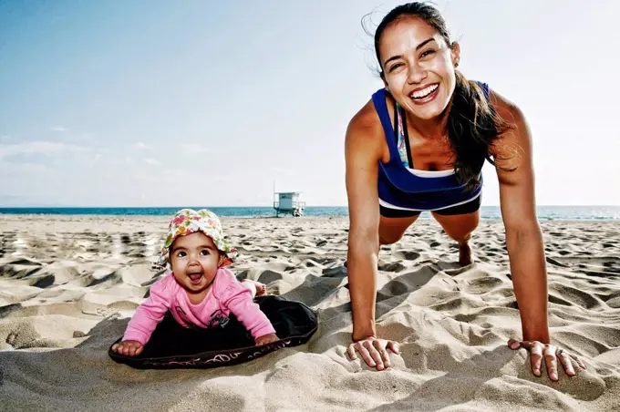 Mother and daughter doing push-ups at beach