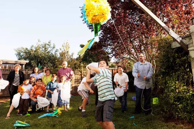 Hispanic family breaking pinata in backyard