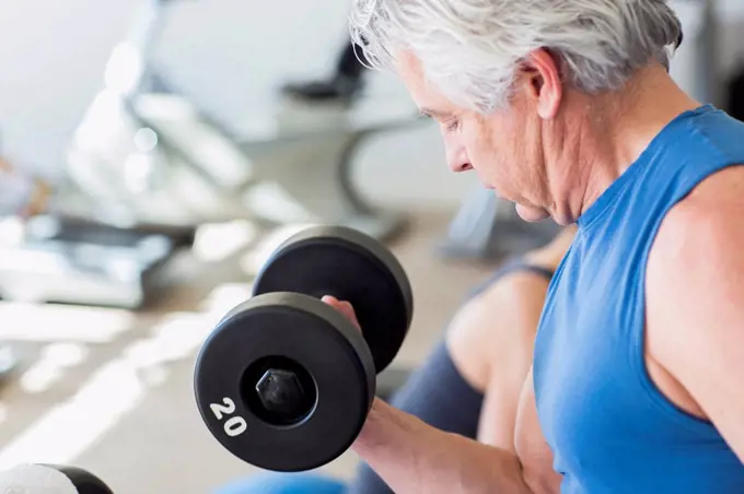 Older Hispanic man lifting weights in gym