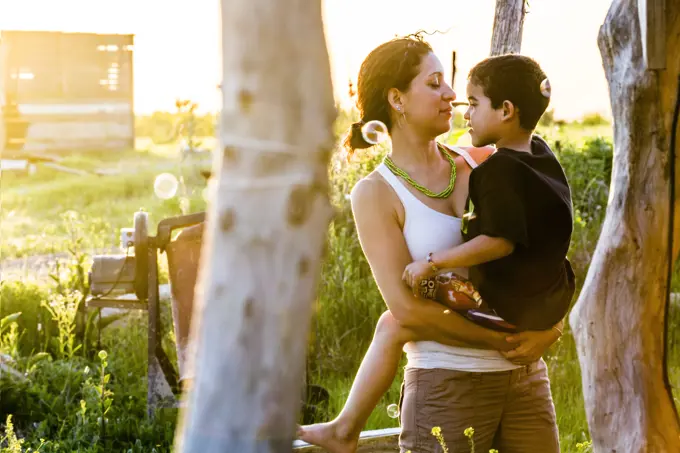 Hispanic mother carrying son in garden