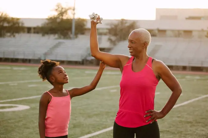 Girl squeezing biceps of grandmother on football field