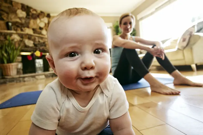 Baby crawling on floor while mother rests from workout