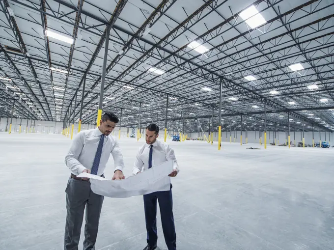 Architects examining blueprint in empty warehouse