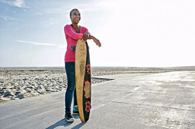 Older Black woman holding skateboard on beach